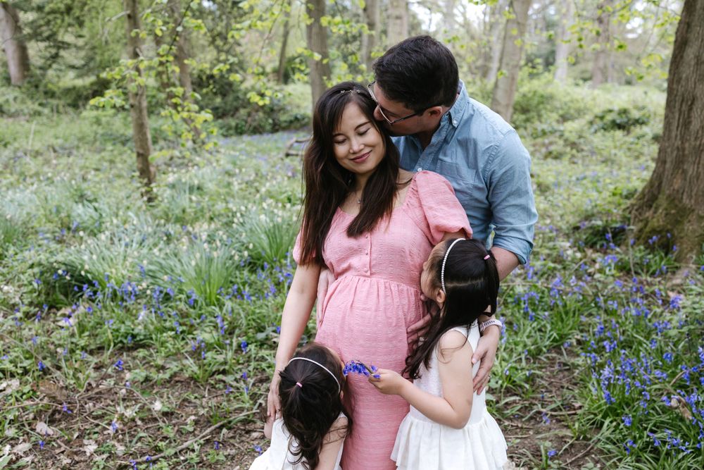 A couple and their daughter share a tender moment surrounded by blooming bluebell flowers in a spring forest.