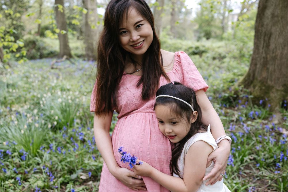A parent and child stand together in a springtime forest with blooming bluebells covering the woodland floor.