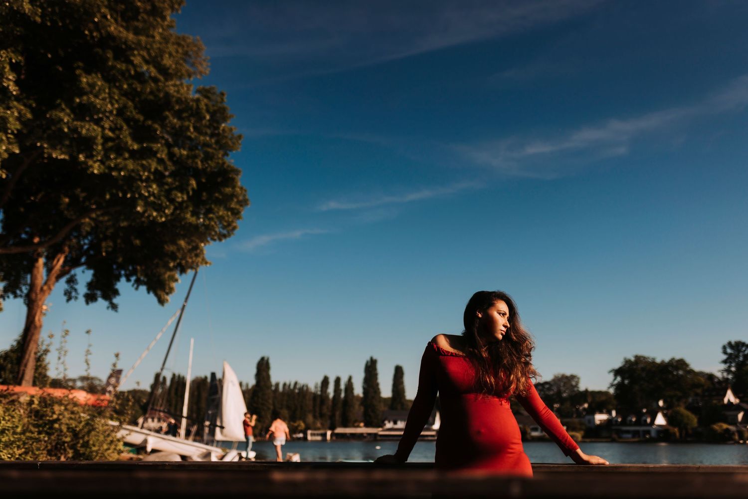 Woman in red dress poses against waterfront backdrop on sunny day.