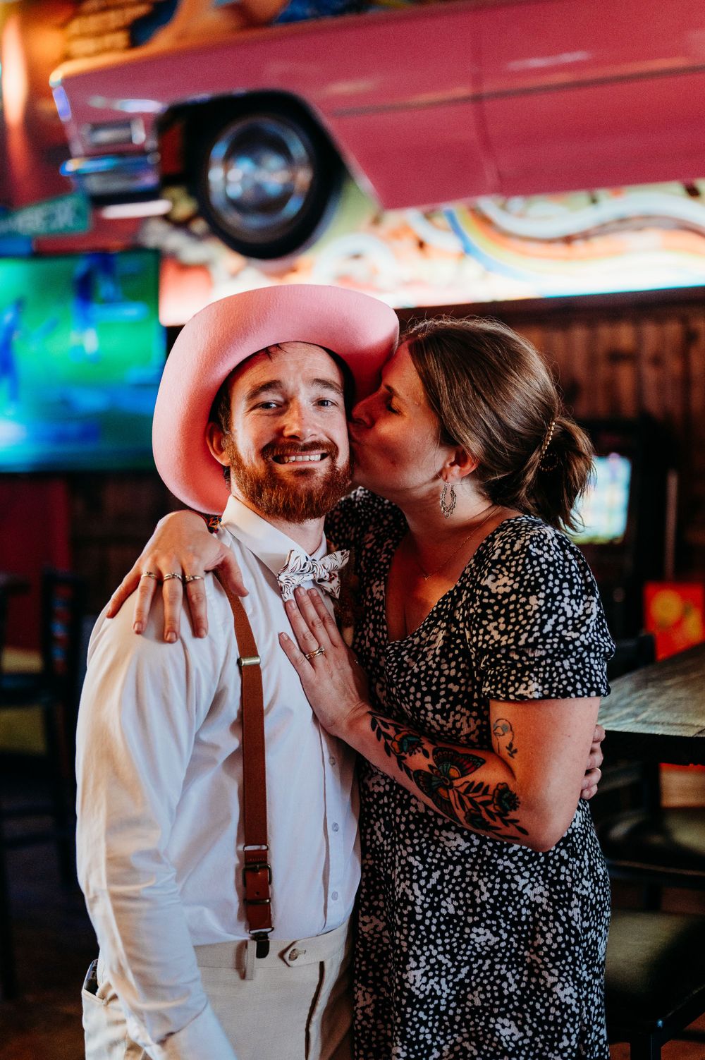 Iowa Midwest photographer kissing husband on cheek in cedar falls iowa bar during party bus stop of wedding. True to life flash photography