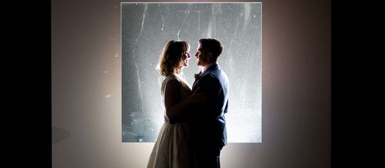 Silhouetted figures in an intimate pose against a bright backlit window.