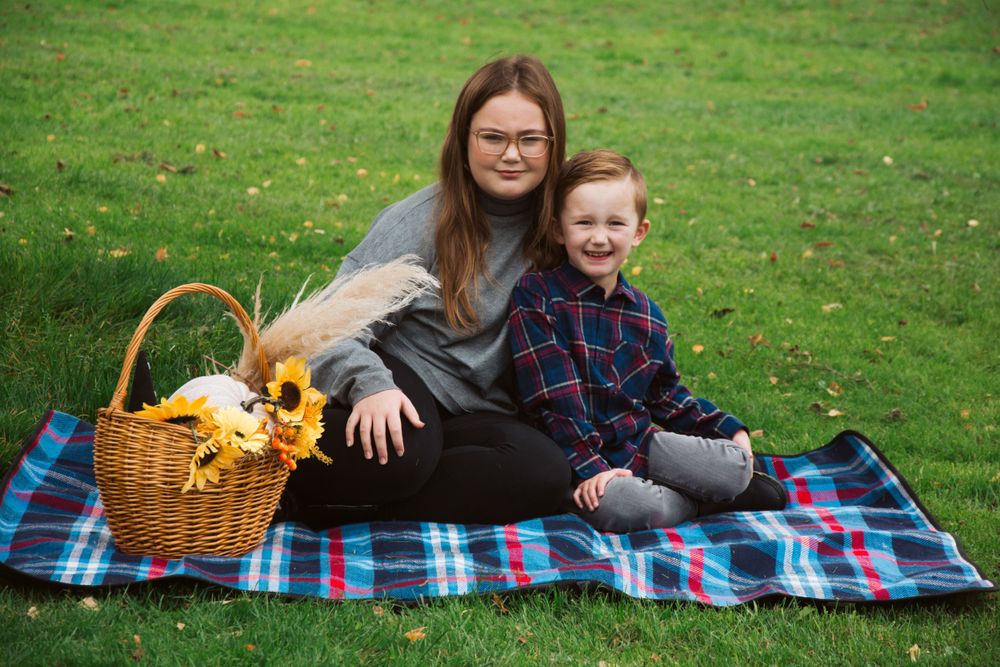 People sitting on picnic blanket with wicker basket of sunflowers on green grass.