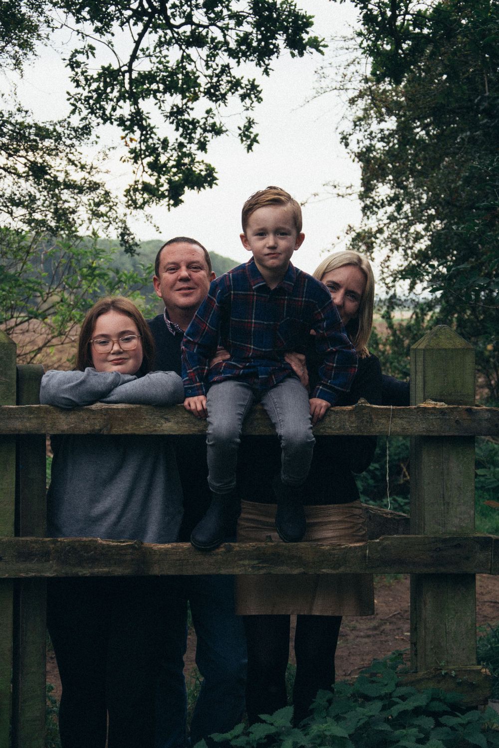 Group portrait of four people sitting on wooden fence in nature setting.