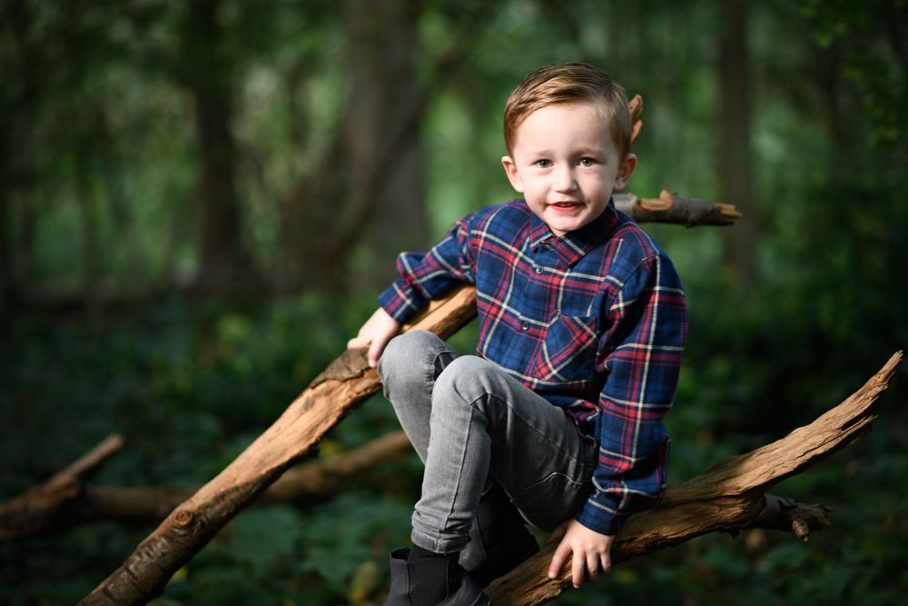 A playful photo of a child in plaid sitting on a fallen tree branch in the forest.