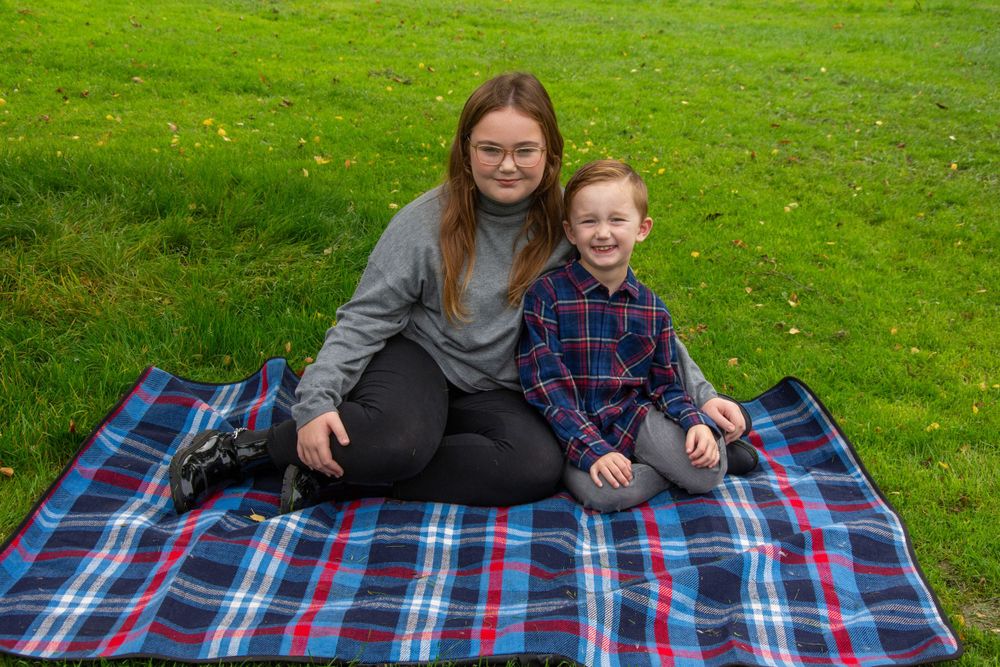 Two people sitting together on blue plaid blanket on grassy lawn.