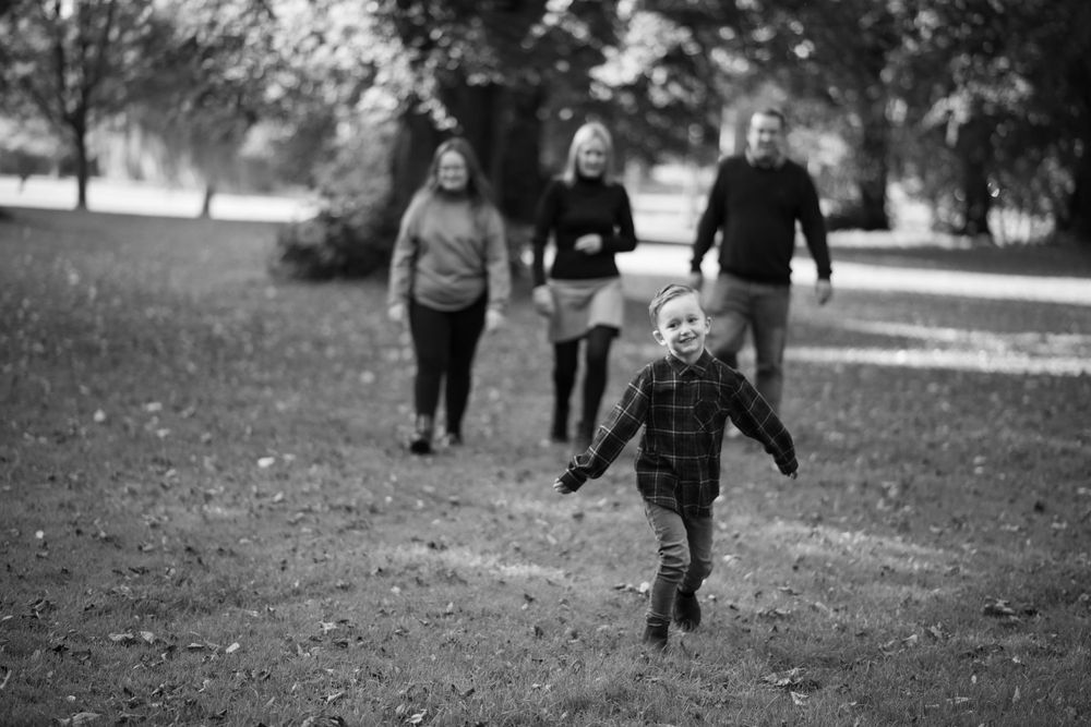 Black and white image of joyful running in park while others follow behind.