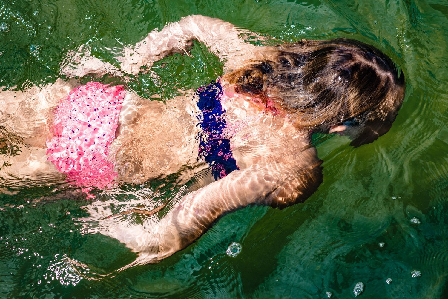 Person swimming in green water wearing pink and purple swimsuit.