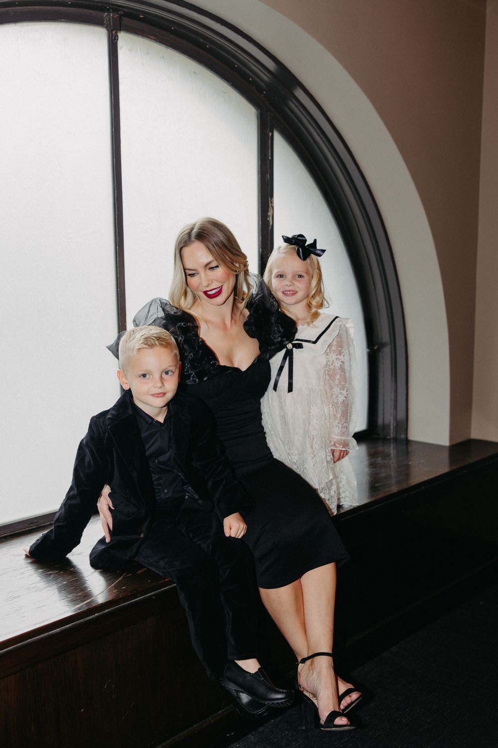 Three people sitting together on a window bench in formal attire sharing a joyful moment.