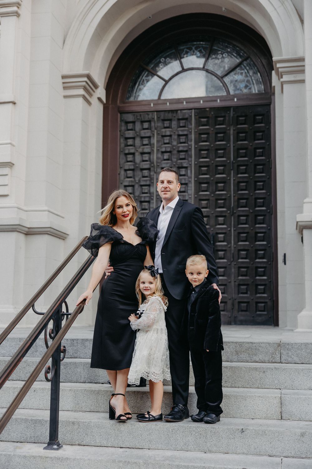 Formal family portrait on stone steps in front of large wooden door.
