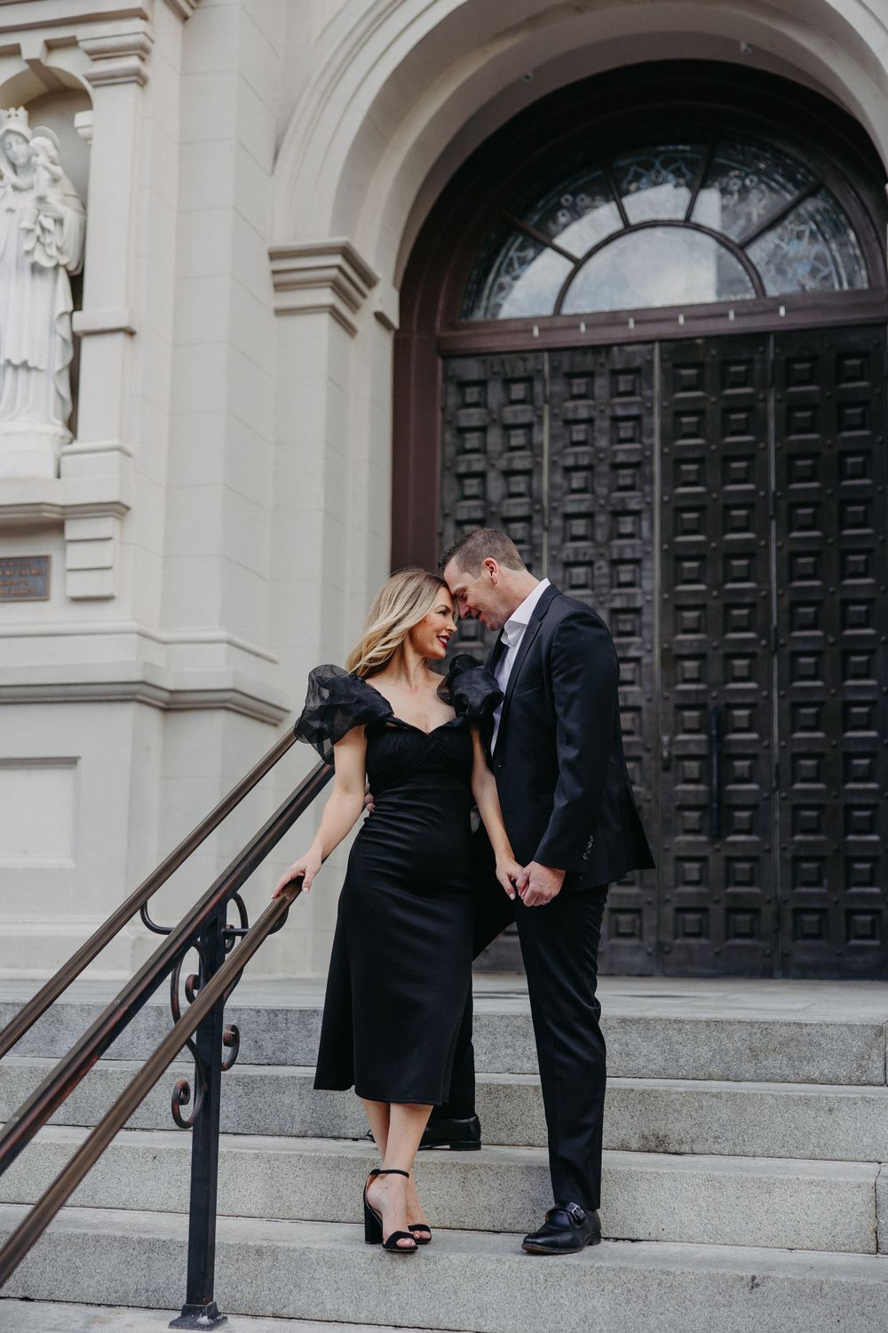 Elegant couple in formal wear sharing an intimate moment on grand stone steps.