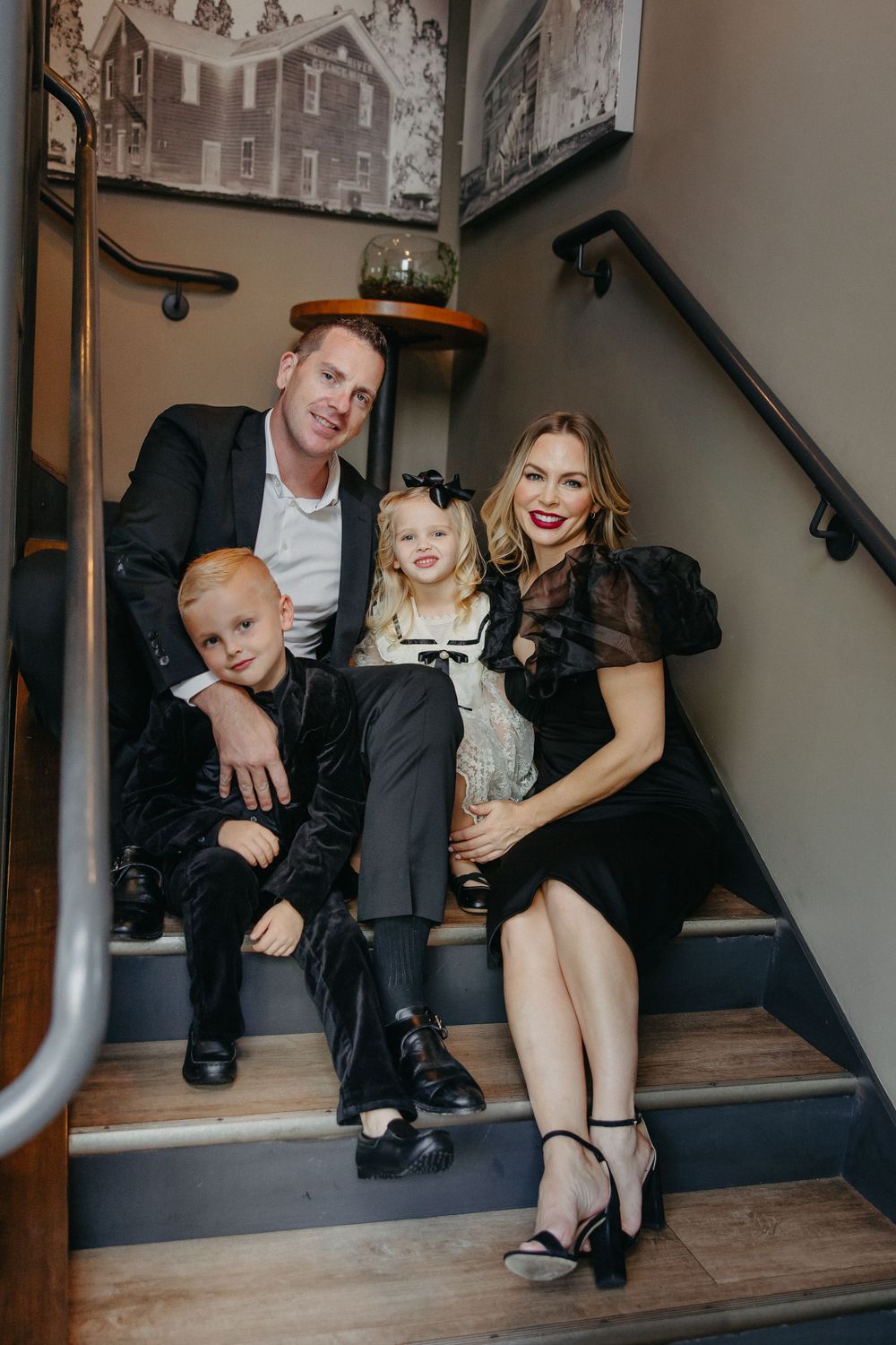 A happy family sitting together on wooden stairs with vintage photographs on the wall behind them.