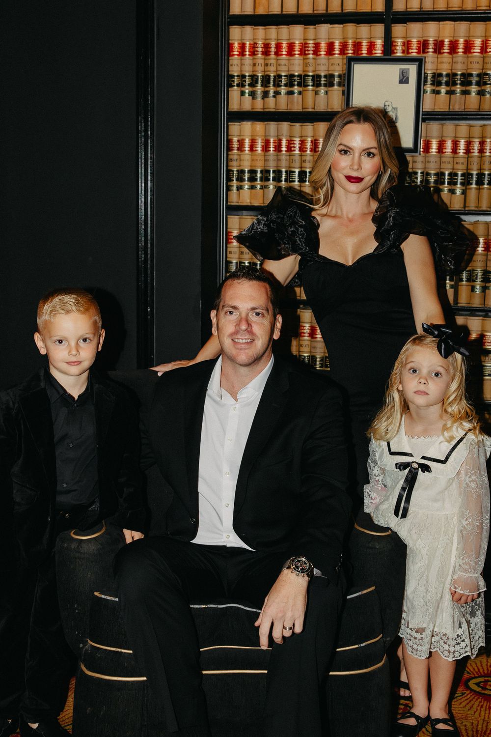 A family portrait in front of a wall of law books, dressed in formal black and white attire.
