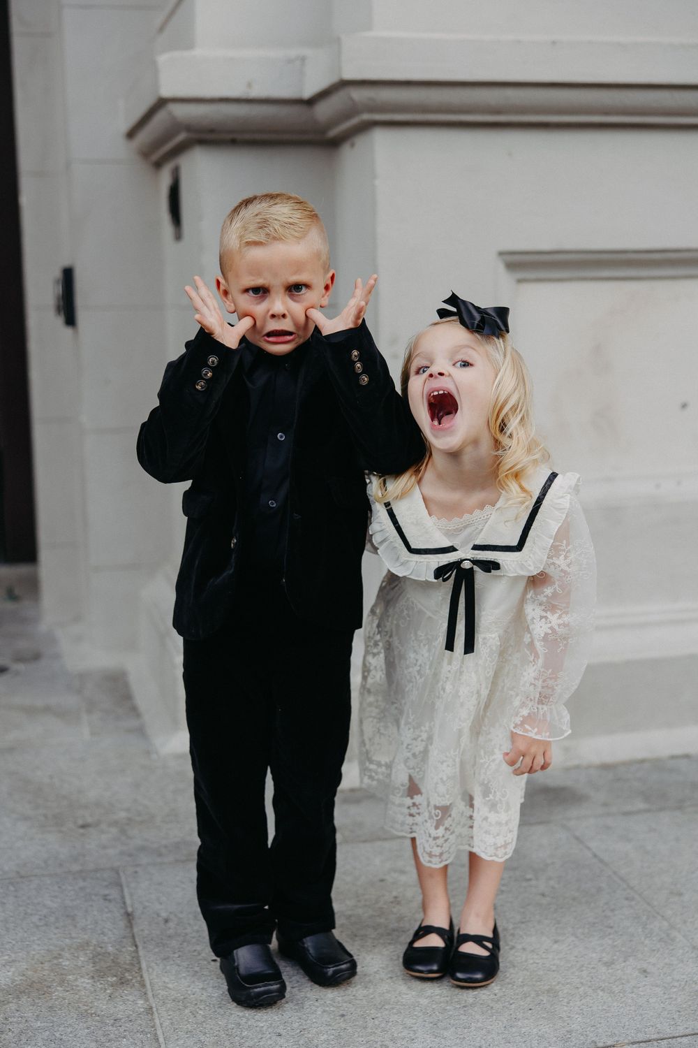 Two children in formal attire making silly faces and posing together on stone steps.