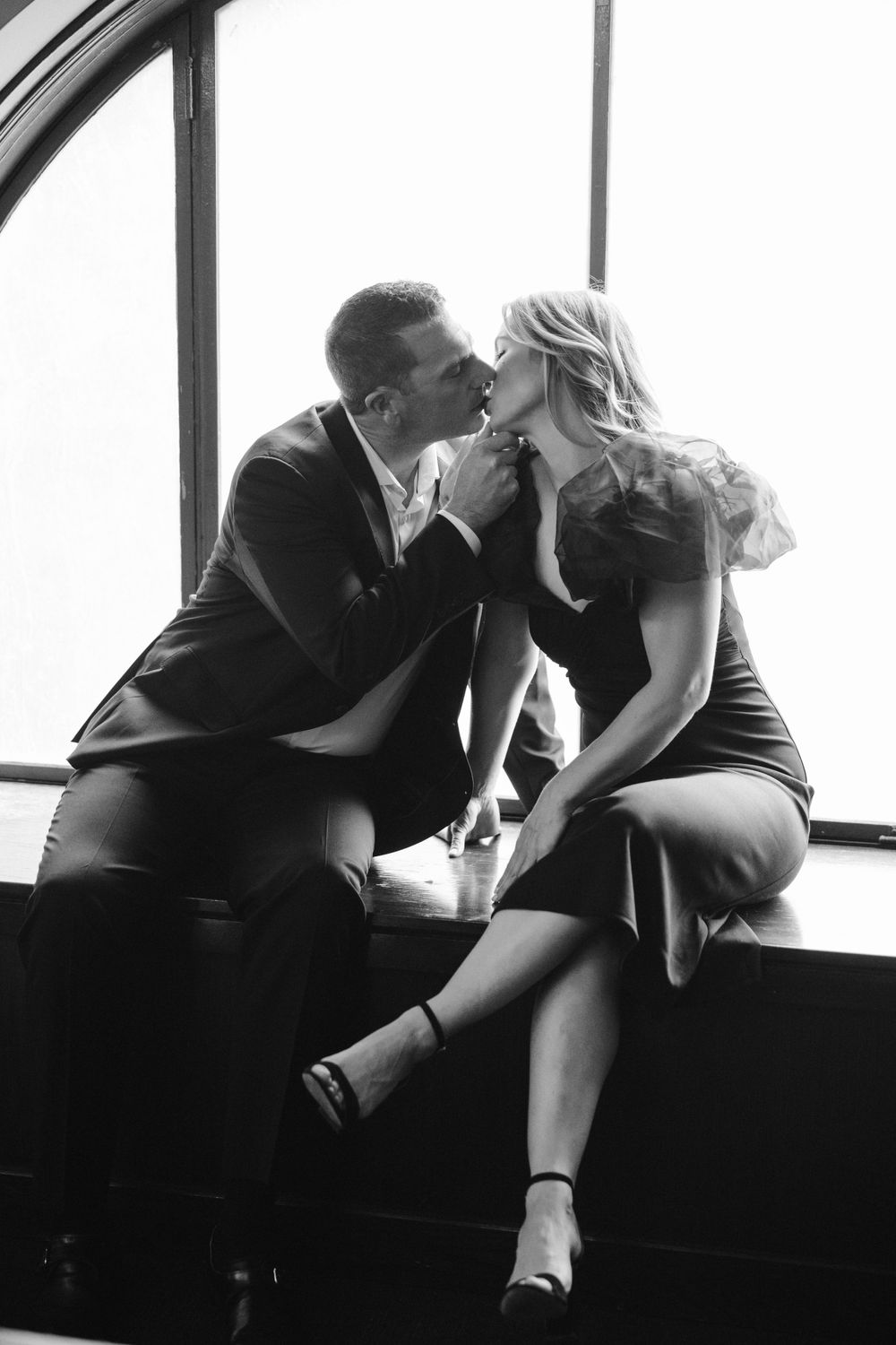 A romantic black and white photo of a couple sharing an intimate moment by a window.