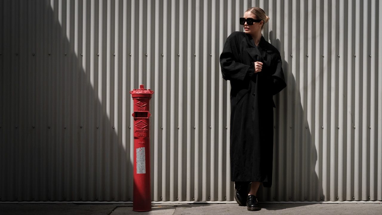 Woman in long black coat and sunglasses against corrugated metal wall, urban portrait, North Vancouver