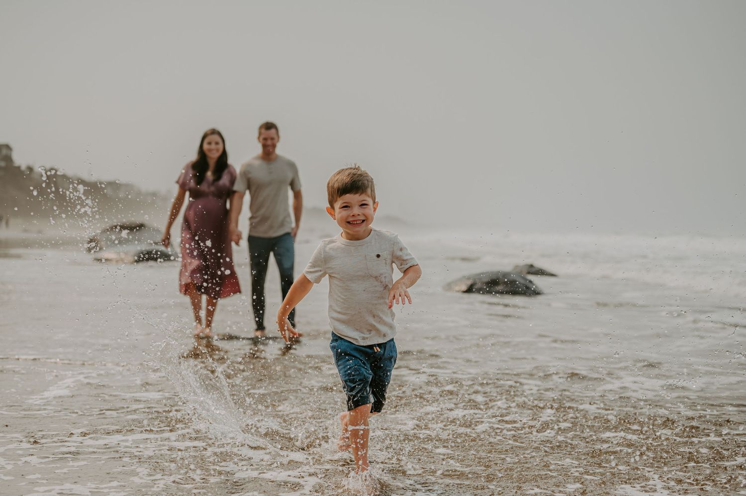Boy runs on the beach with his family behind