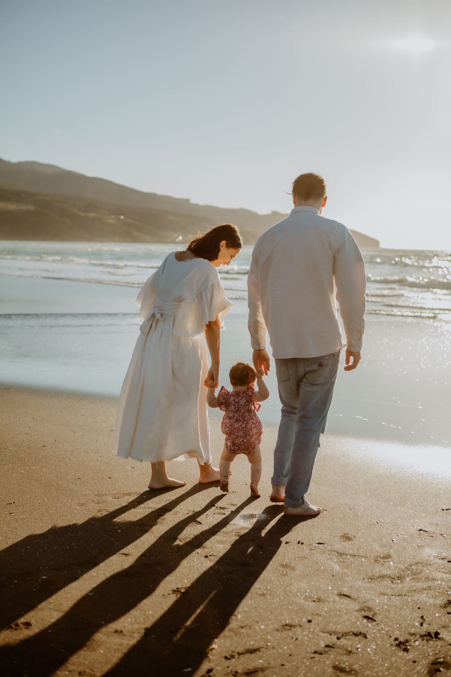 A family walks along a beach at sunset casting long shadows in the sand.