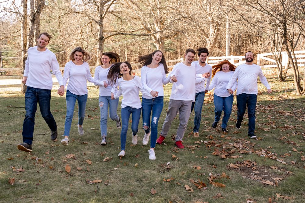Fun group photo of people in white shirts and jeans jumping together in a park.
