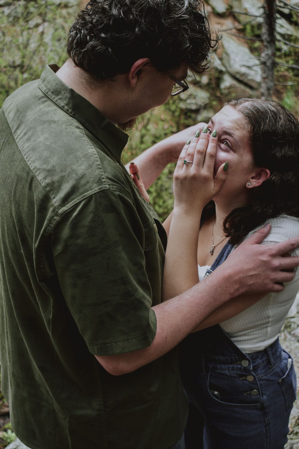 Couple sharing an emotional embrace near rocky terrain during outdoor engagement session.