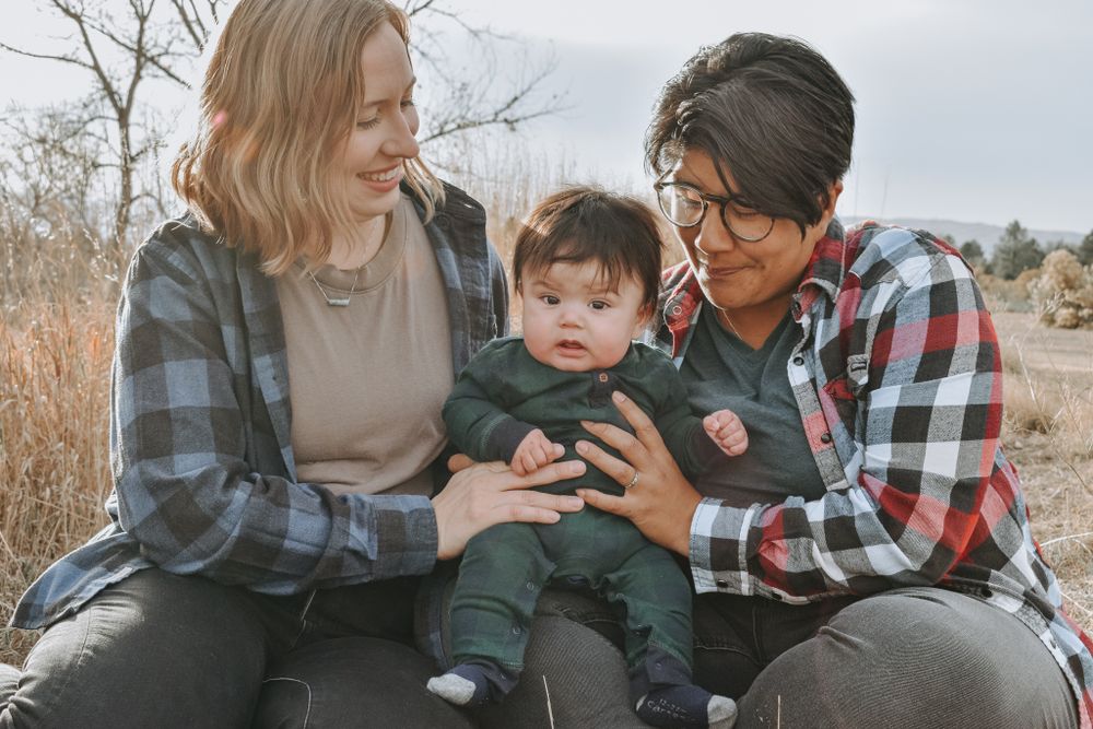 Young interracial couple sitting outdoors in a field holding their infant baby.