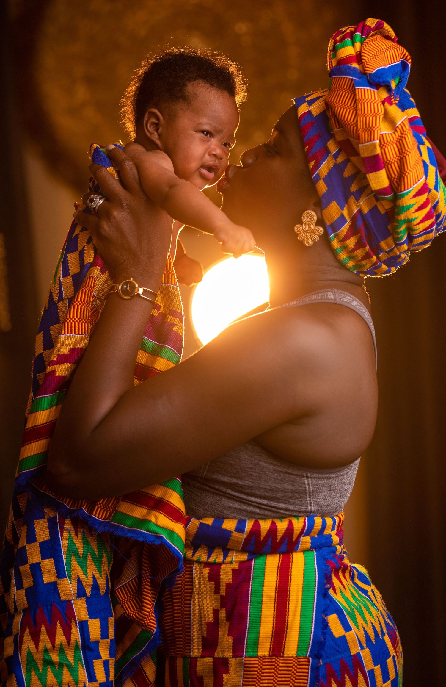 Person wearing vibrant African print fabric poses in warm candlelit setting.