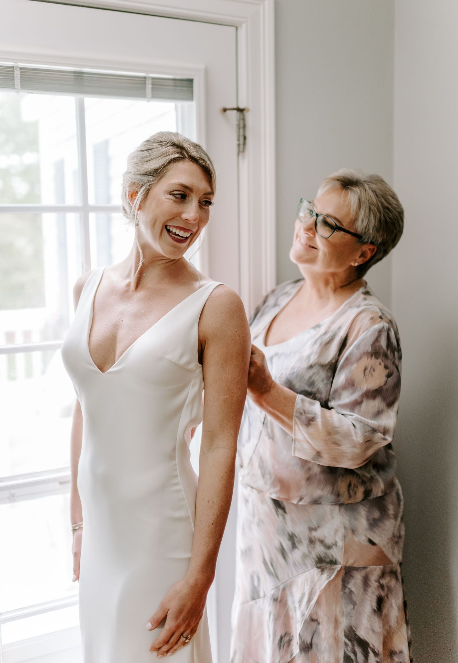 Two people share a candid moment in a bright room with white walls and natural lighting.