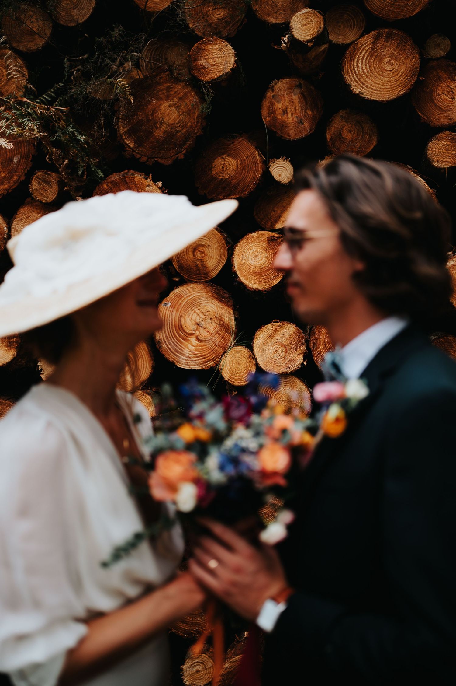 A close-up moment between newlyweds with colorful bouquet against stacked logs.