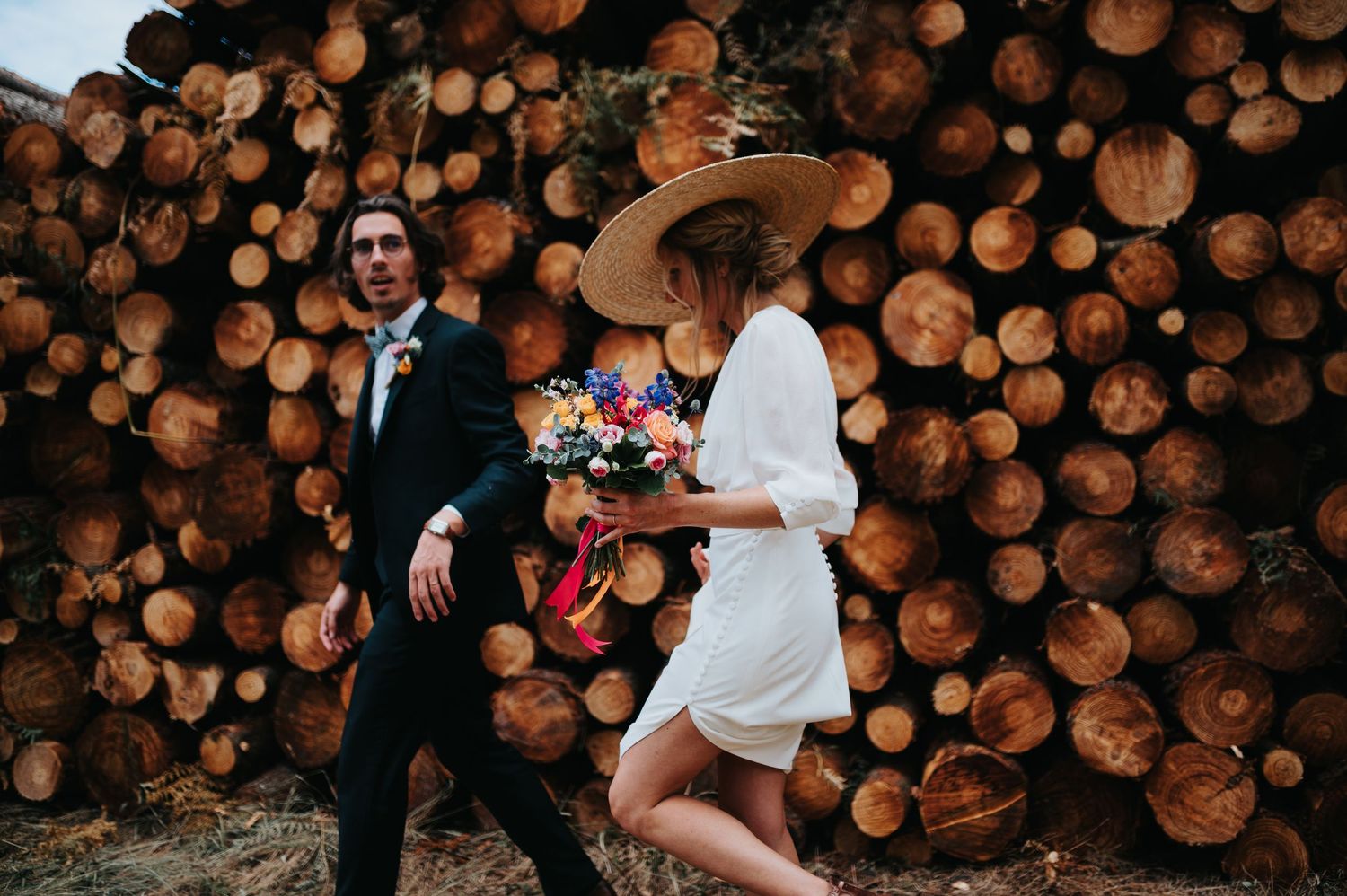 Wedding party members dance and celebrate in front of rustic wood pile backdrop.