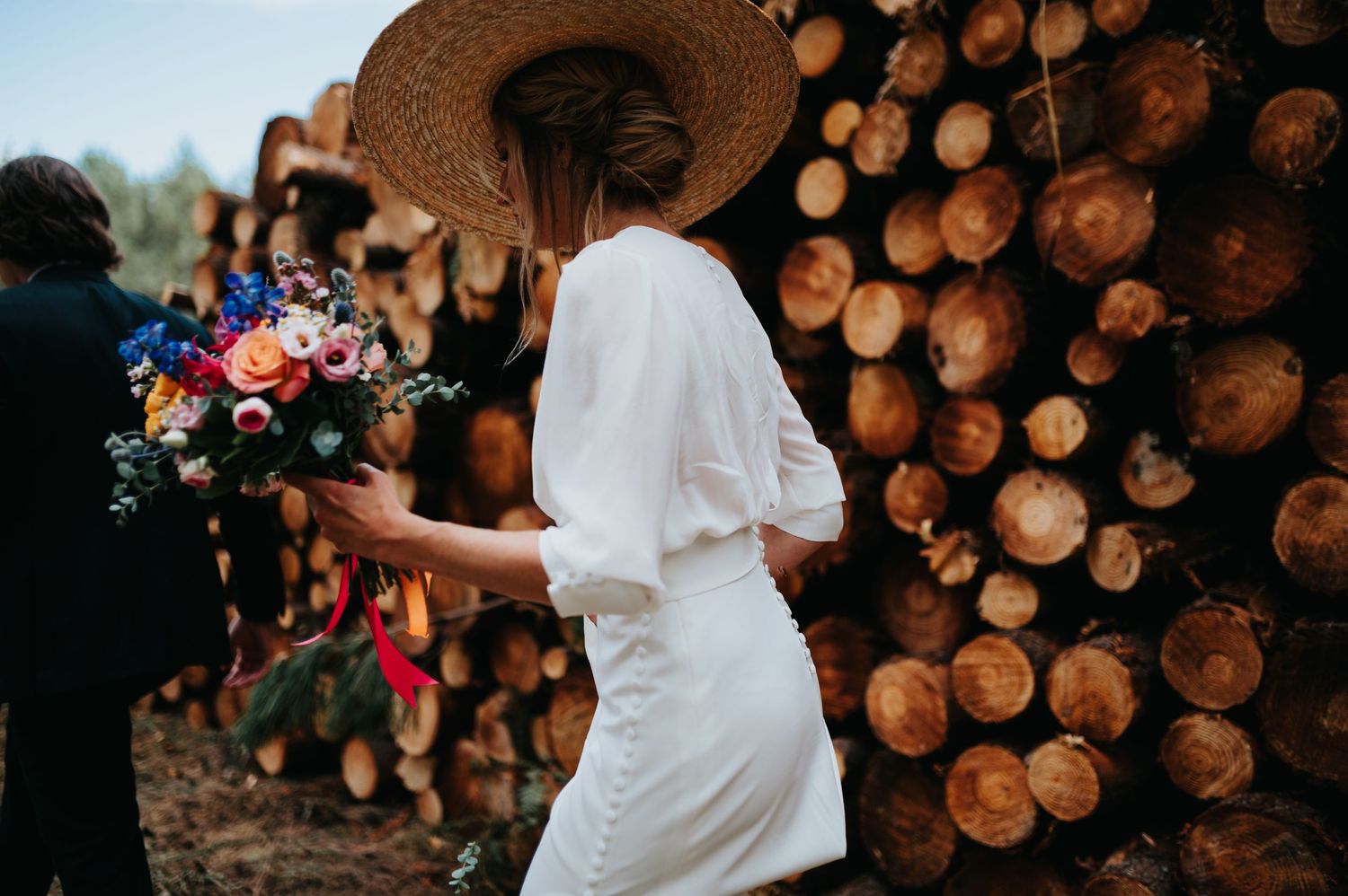 A couple poses in front of stacked logs at an outdoor wedding venue.