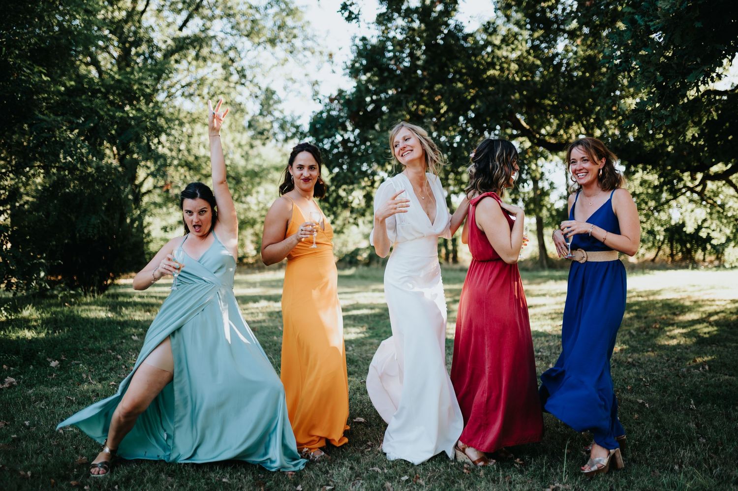 Group in vibrant bridesmaid dresses laughing together in garden setting.