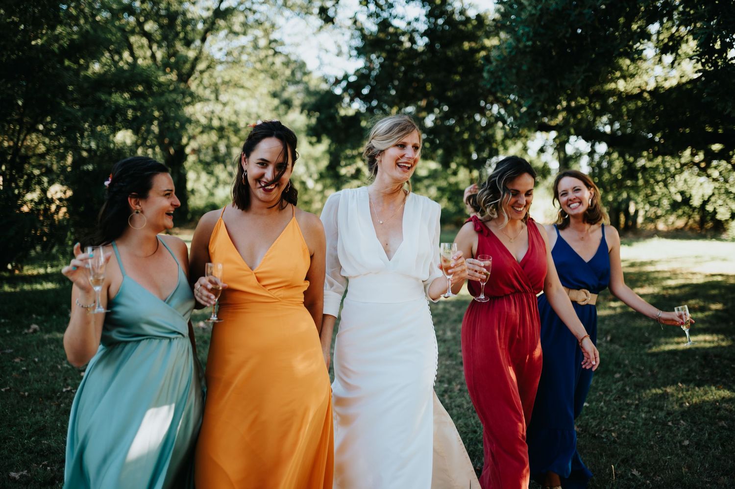 Wedding party members in colorful dresses pose together outdoors.