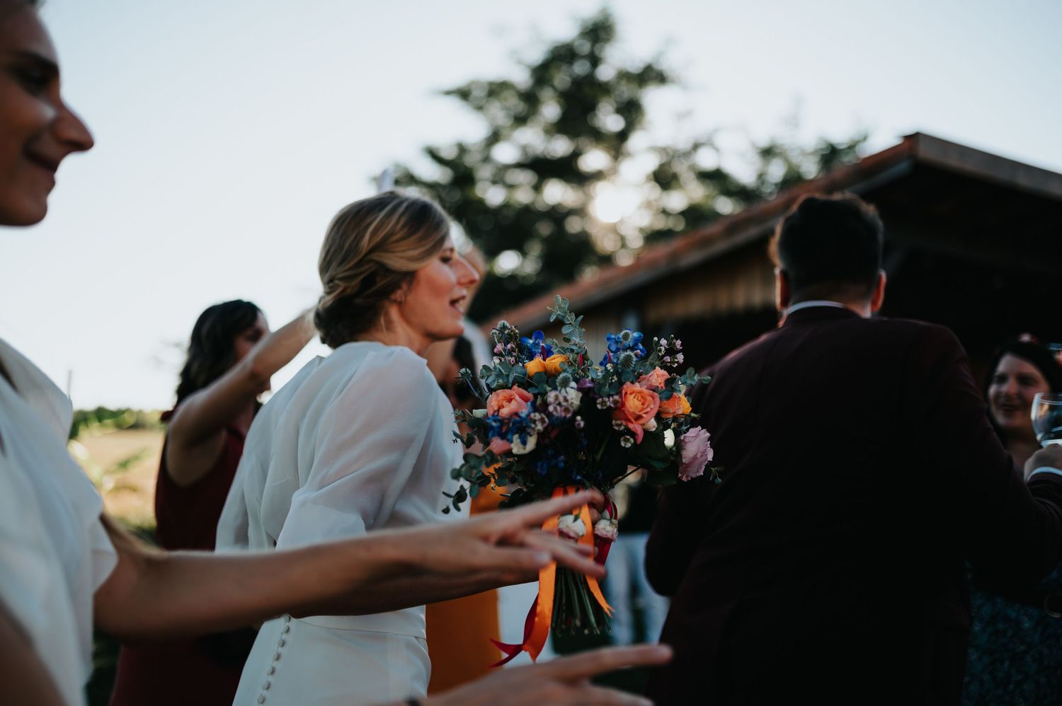 Wedding guests dancing and celebrating at an outdoor reception during sunset.