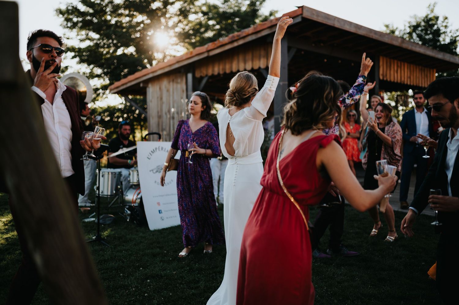 Festive outdoor wedding reception with guests dancing near a rustic building.