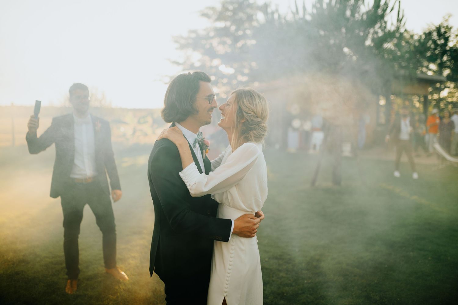 Wedding guests gather outdoors in a misty sunset atmosphere.