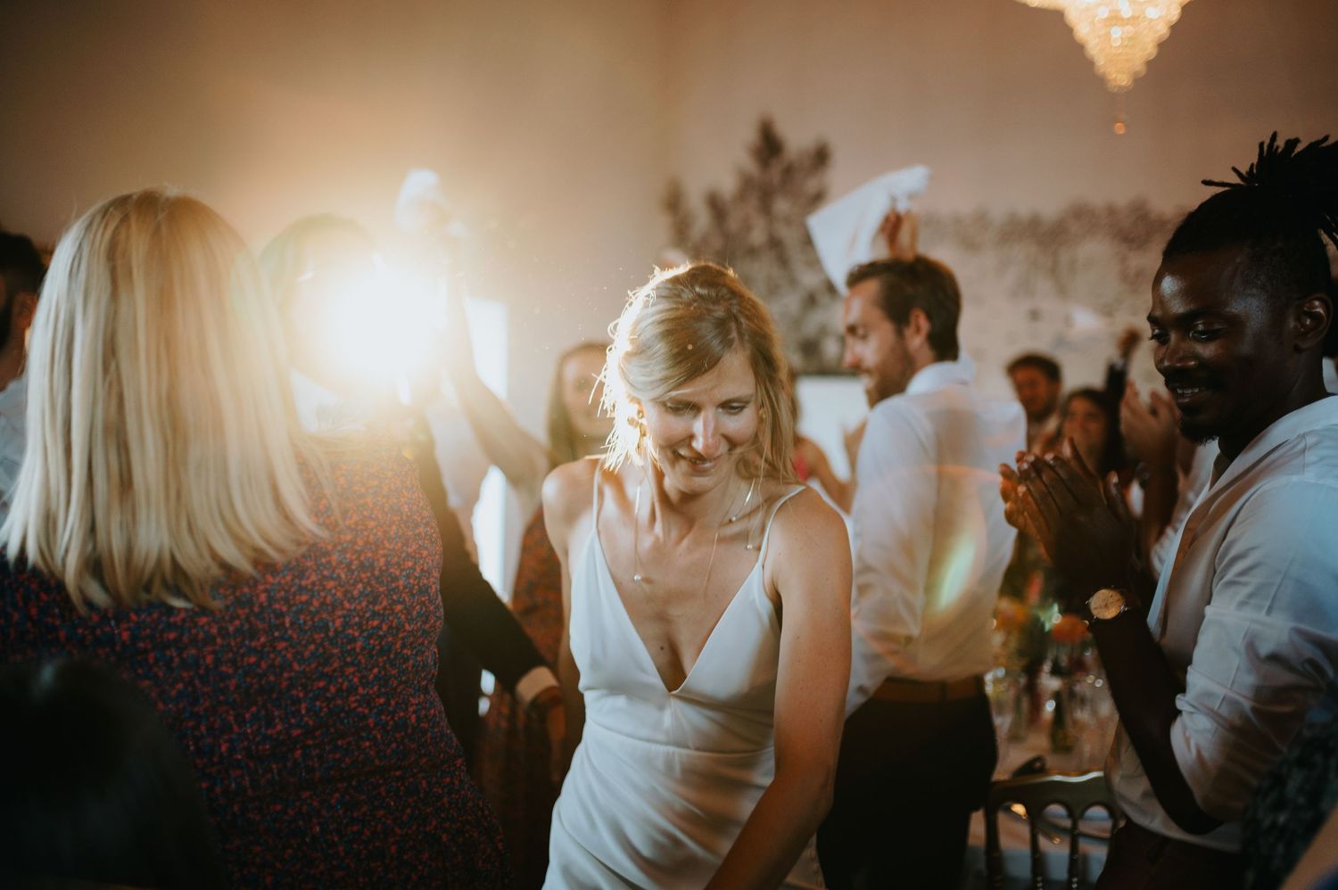 Wedding reception dance party with chandelier lighting and joyful atmosphere.