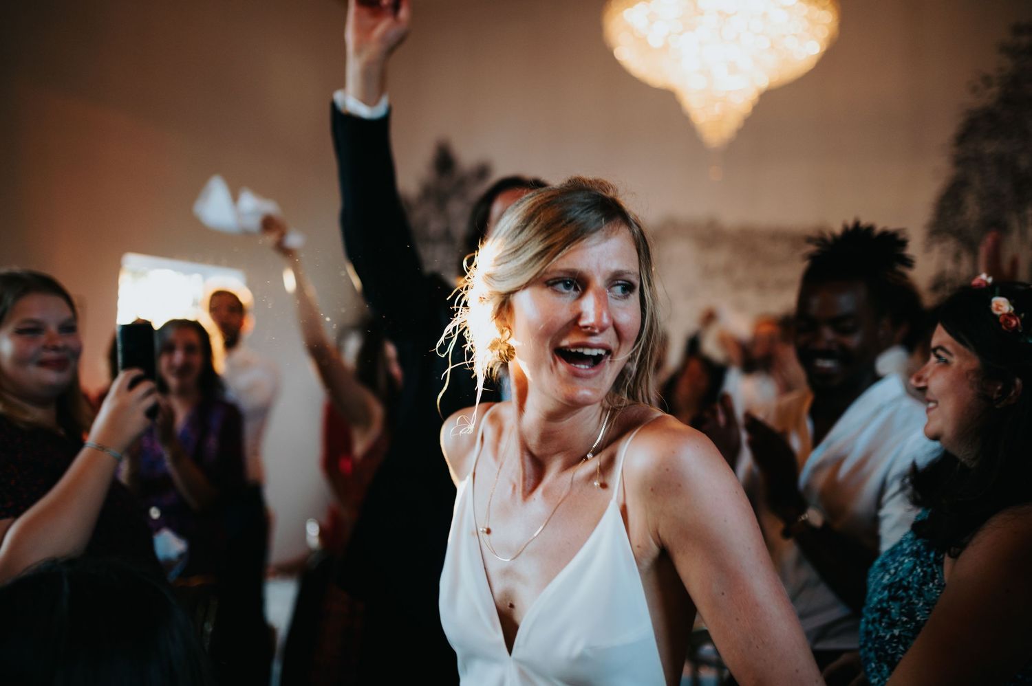 Energetic dance floor scene at an indoor wedding reception with warm lighting.