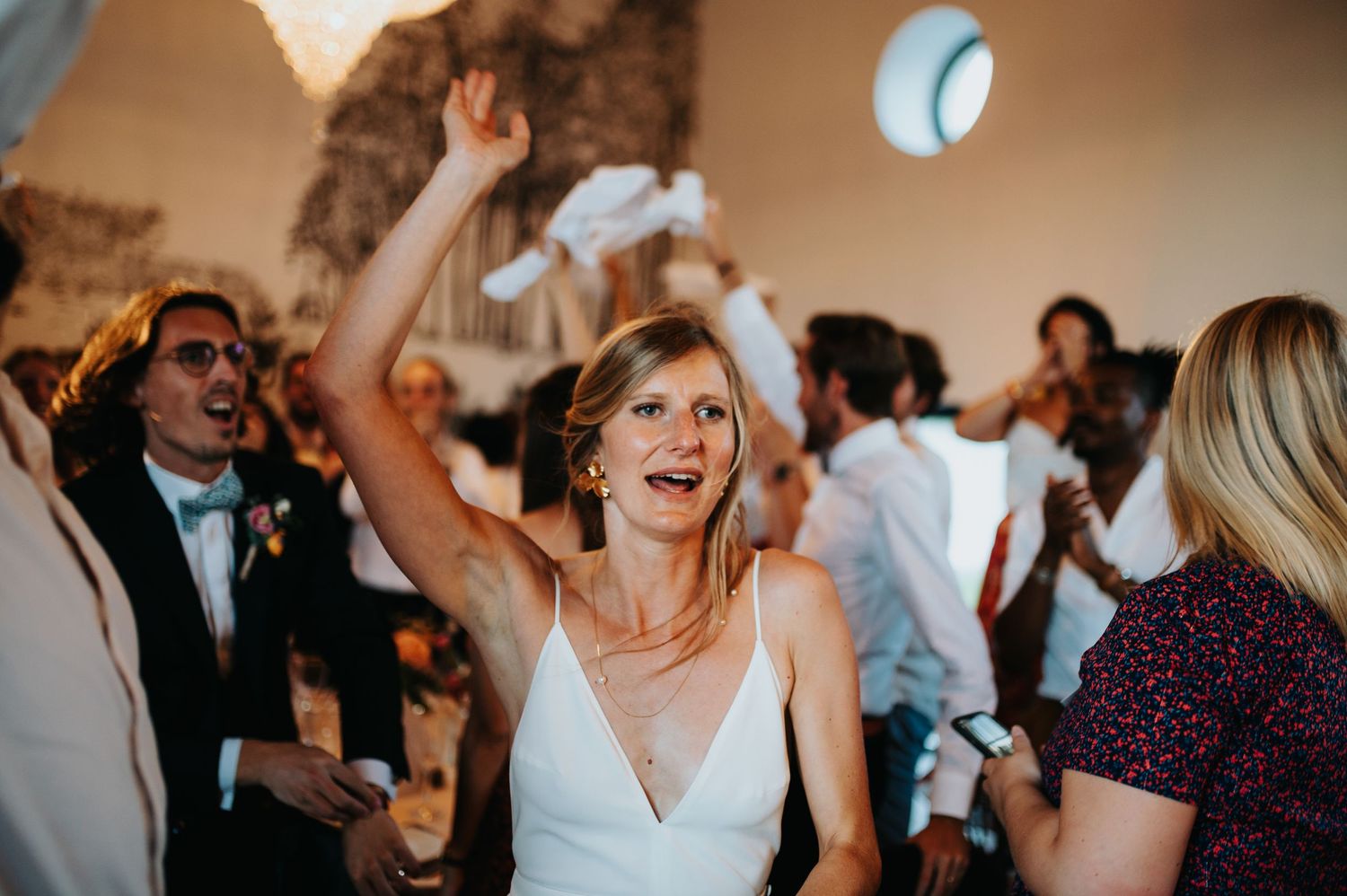 Lively wedding reception with guests dancing under crystal chandeliers.