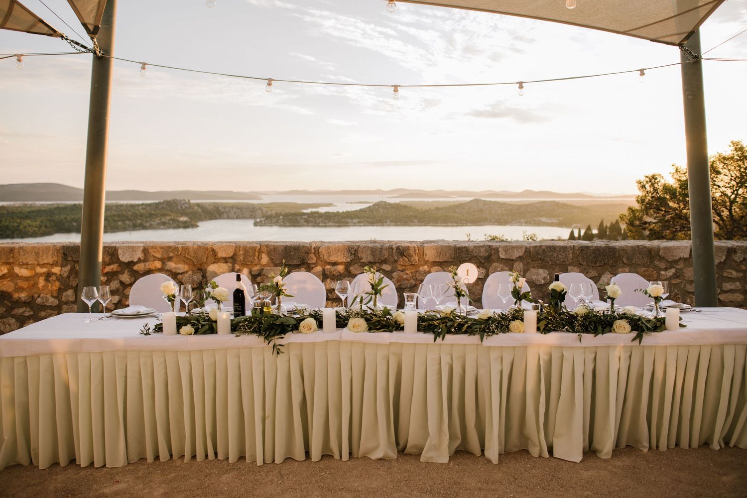 Elegant wedding reception table setup with white linens and decor overlooking a scenic sunset landscape view.