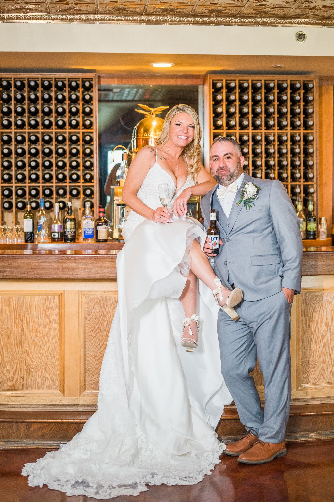 Happiness radiates as the couple looks at the camera, with the bride seated at the bar.