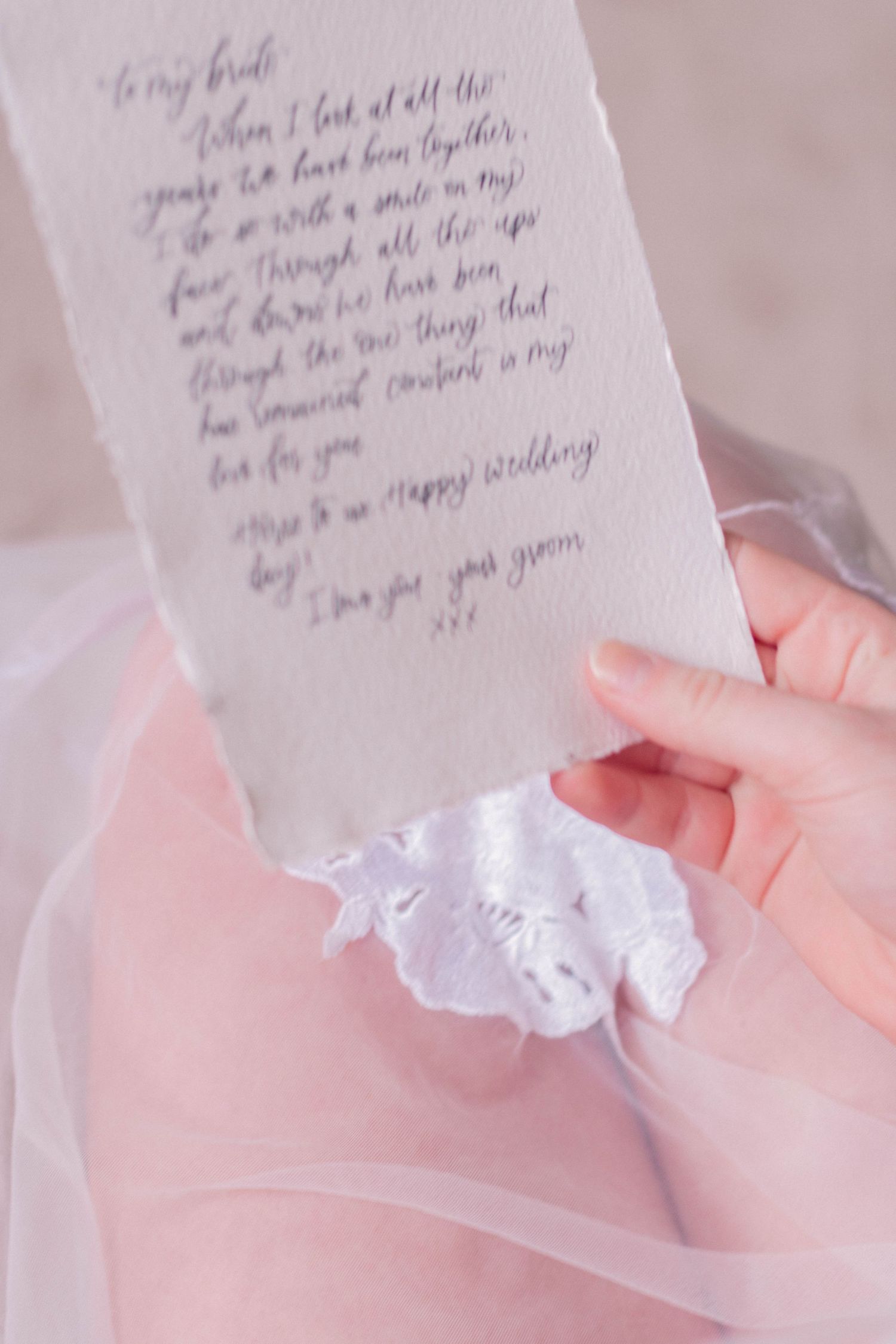 A handwritten wedding note on delicate paper with soft pink fabric in the background.