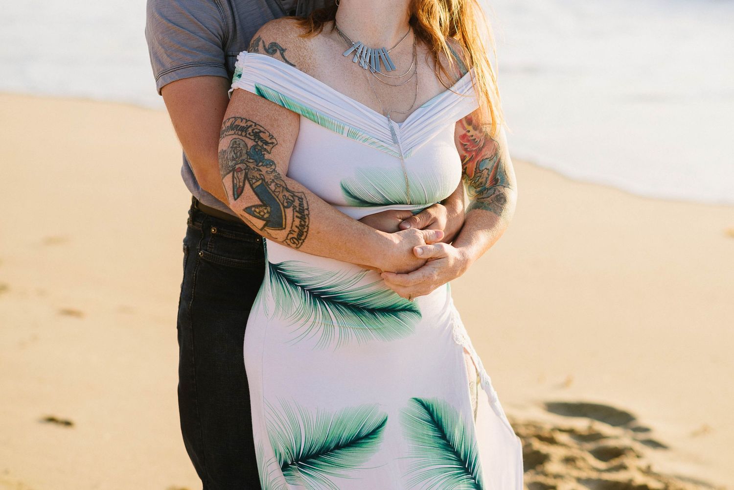 Close-up of a couple embracing in a white and green palm leaf dress on the beach.