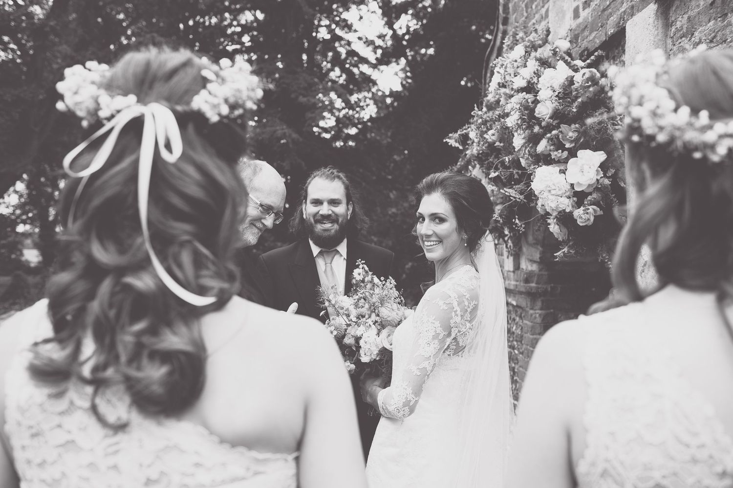 Black and white photo of a wedding ceremony with bridesmaids in floral headpieces.