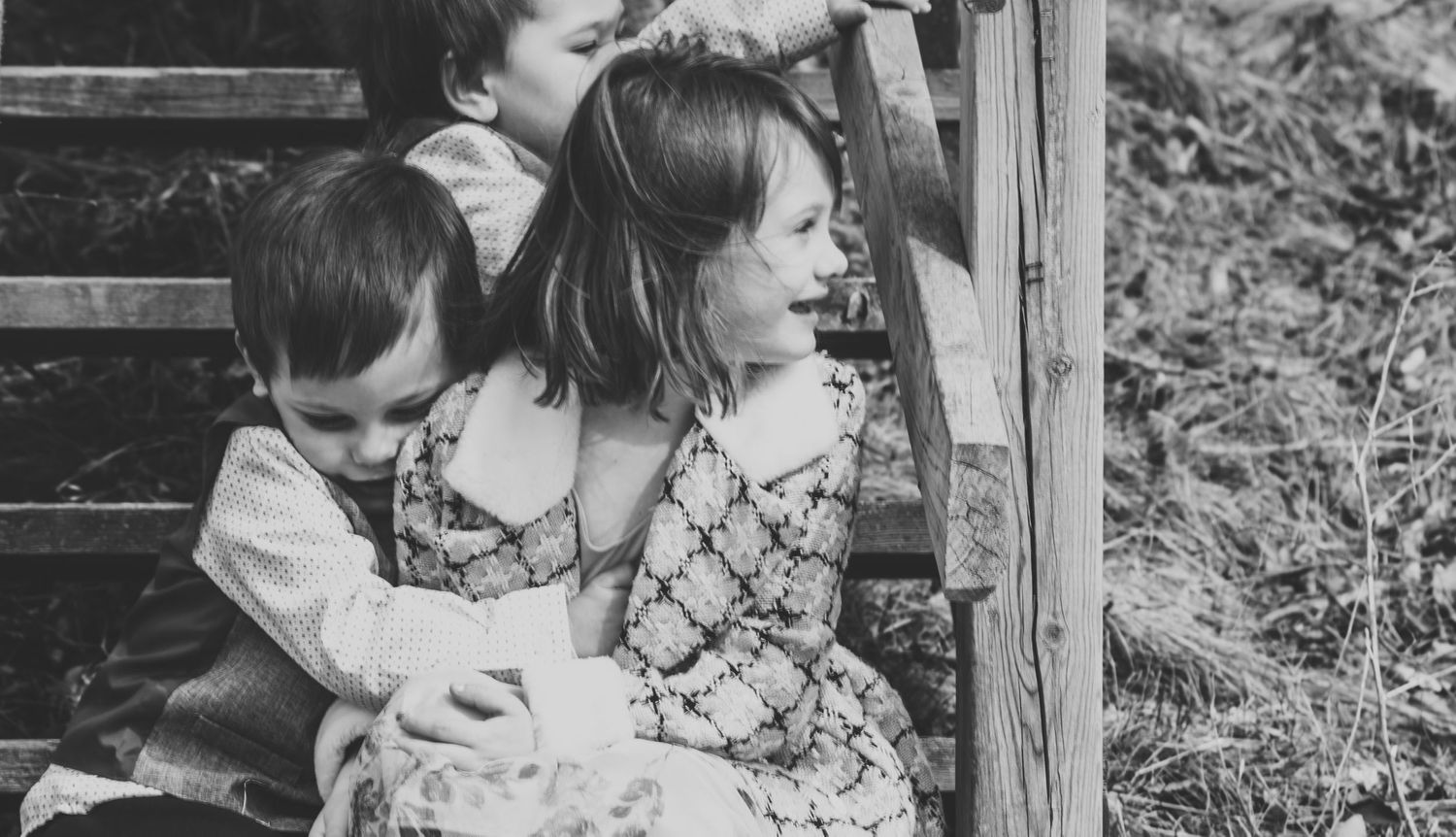 Children sitting together on wooden steps in a black and white photograph.