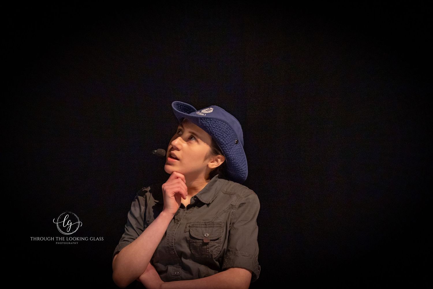 Performer in blue baseball cap strikes thoughtful pose during theatrical scene.