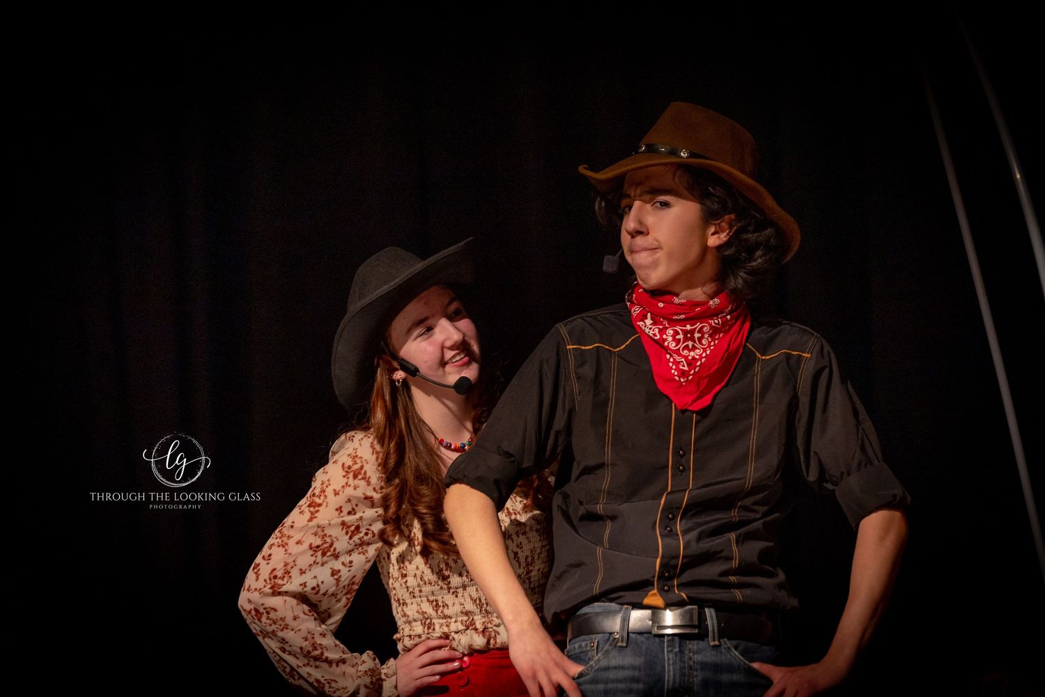 Two actors in Western costumes perform dramatic scene together on dark stage.