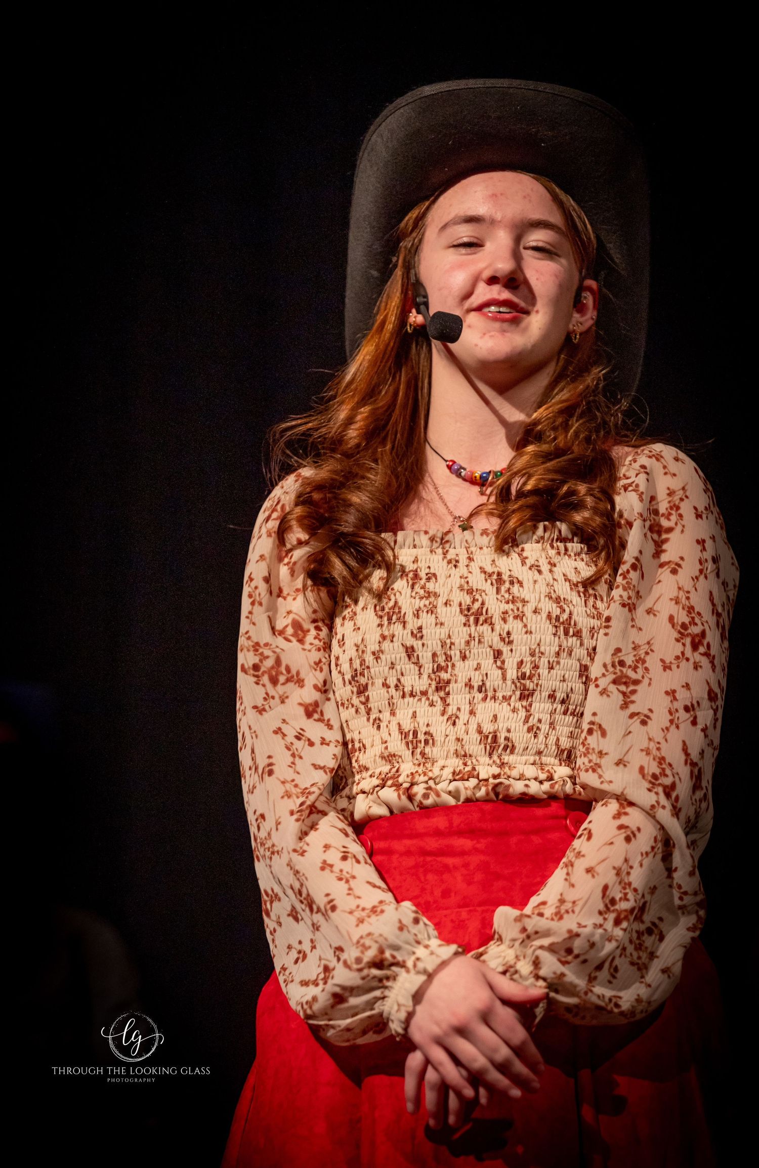 Stage performer in vintage dress and cowboy hat with microphone headset.