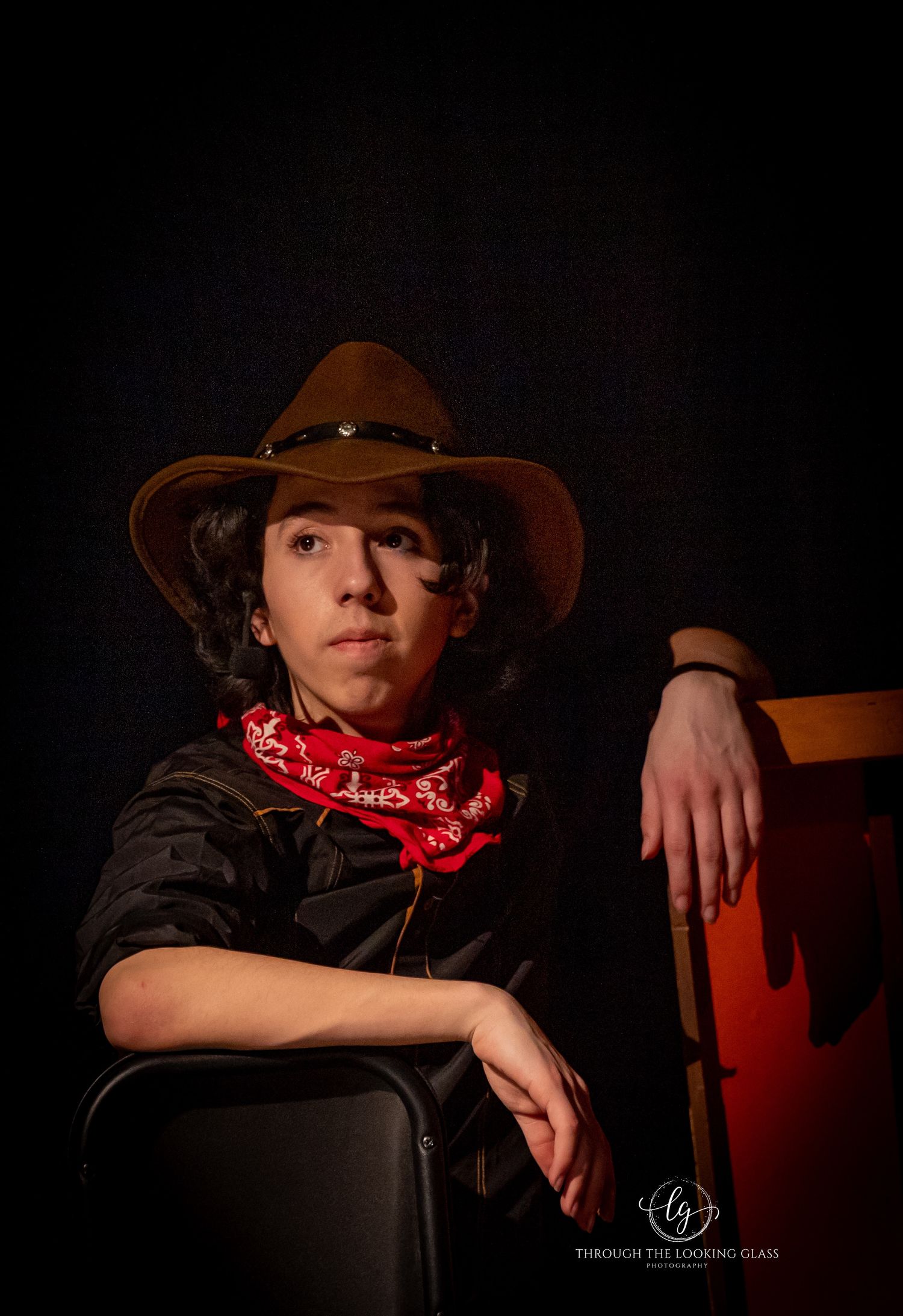 Western-styled portrait with cowboy hat and red bandana against dark background.
