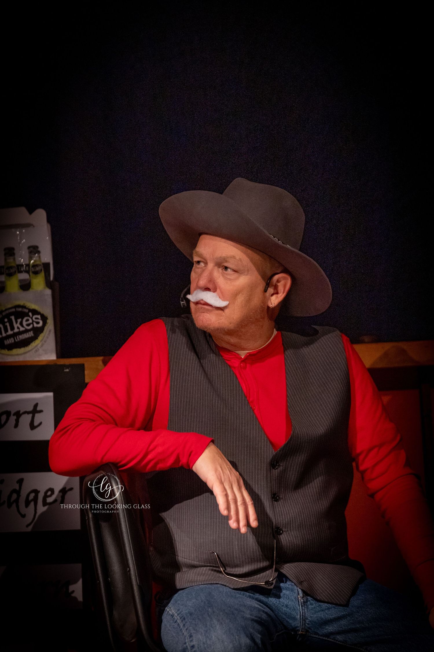 Performer in cowboy hat, red sweater and vest poses dramatically against dark background.