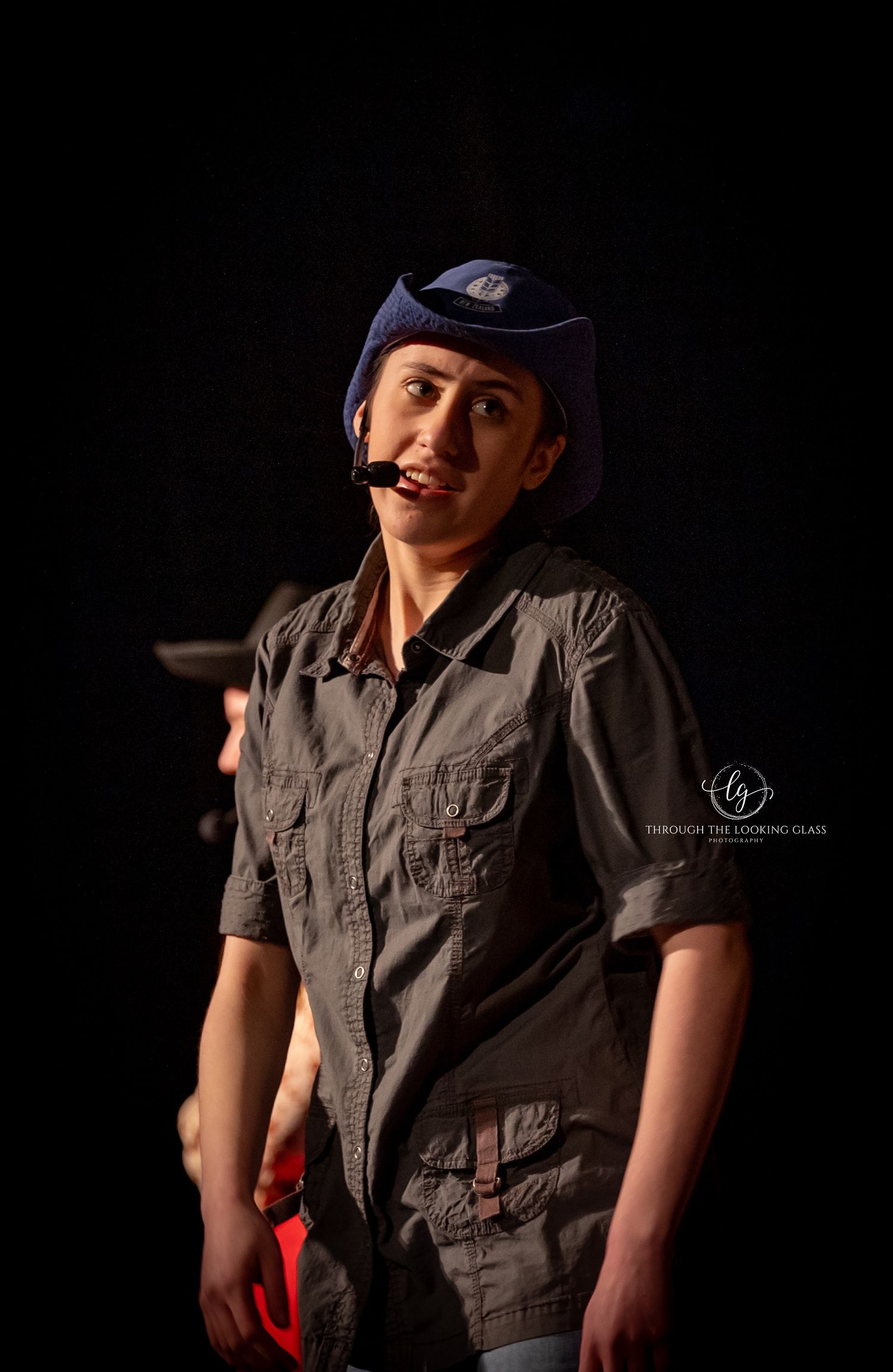 Performer in work uniform and cap delivers dialogue during theatrical production.