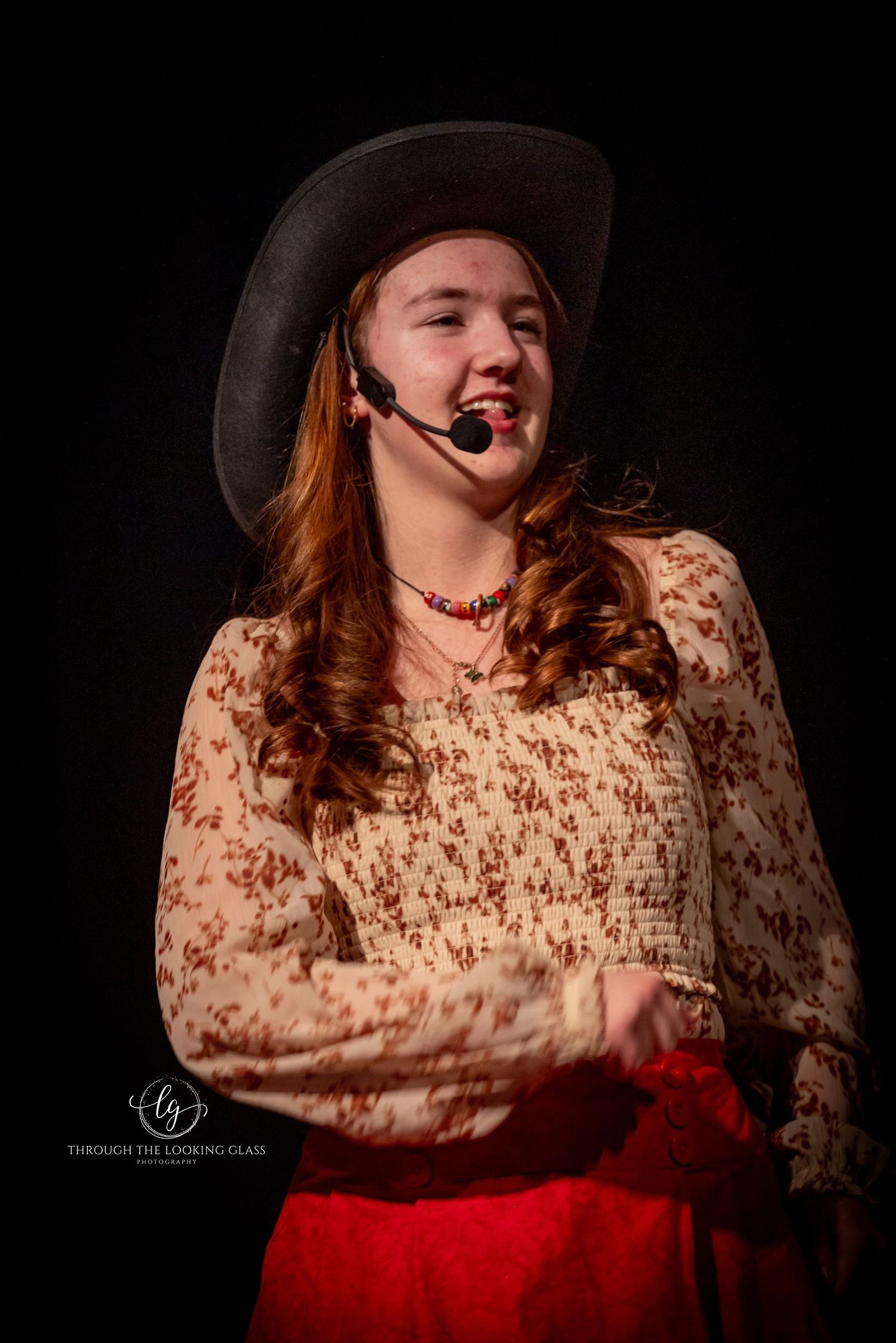 Performer in western costume with cowboy hat and floral print dress gestures during stage show.